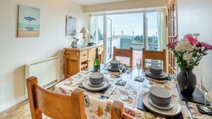 Un coin repas avec une table dressée pour quatre personnes, un buffet en bois et une vue sur l’extérieur.