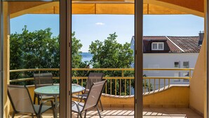 Ein Balkon mit Glastür, Tisch und Stühlen sowie Blick auf ein Gebäude und Bäume.