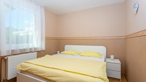 Ein Schlafzimmer mit einem Bett, einem Nachttisch, einem Fenster mit leichtem Vorhang und einer Heizung.