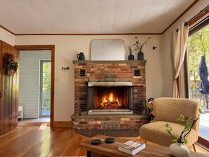 A living room with a brick fireplace, a comfortable beige armchair, and a wooden coffee table.