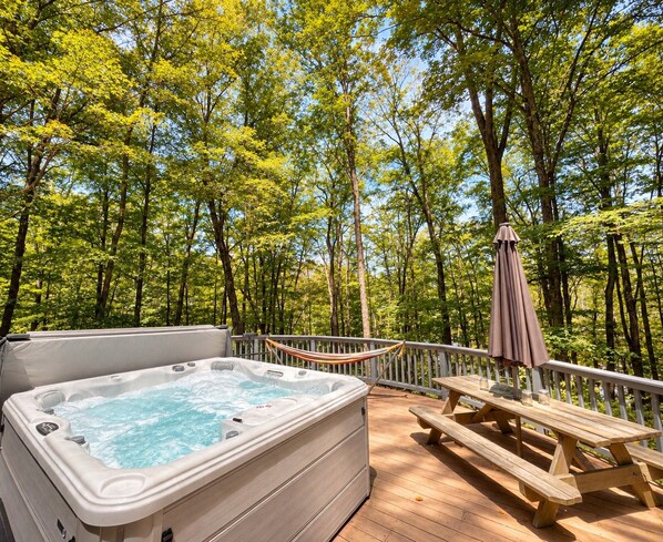 A hot tub on a wooden deck surrounded by trees.