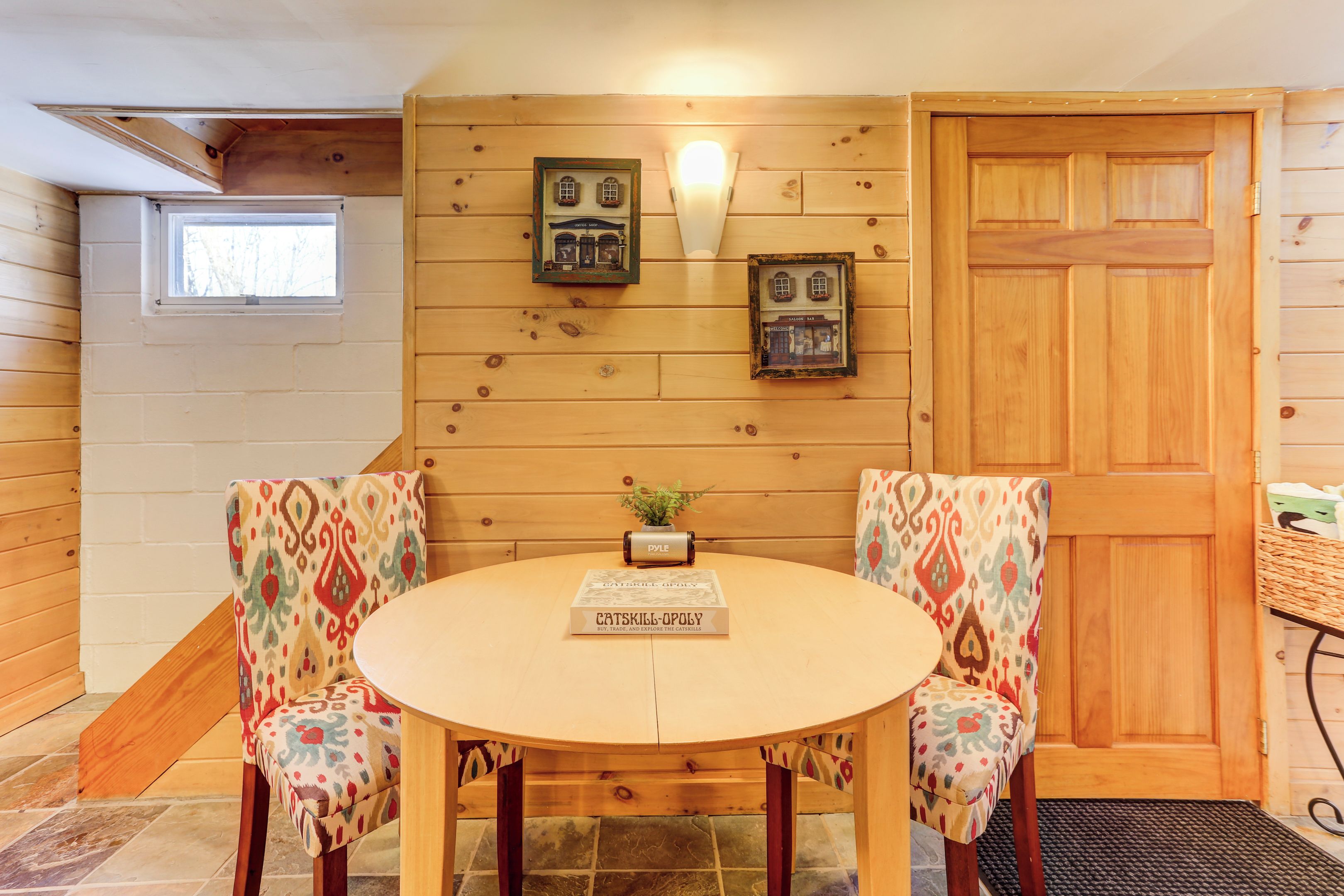 A cozy room with wooden walls, a round table, two patterned chairs, a door, and a window.