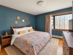 Une chambre à coucher comprenant un lit, des tables de chevet, une commode et une fenêtre donnant sur la forêt.