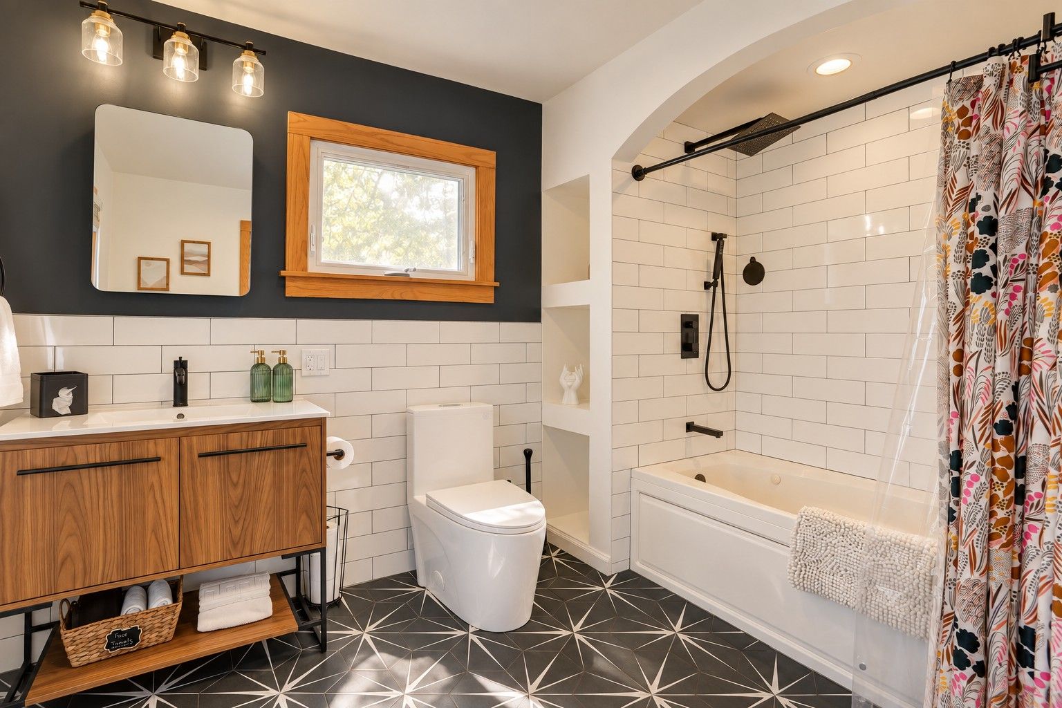 Une salle de bain moderne avec des toilettes blanches, un meuble-lavabo en bois, une douche avec un tuyau noir et un rideau de douche à motifs.