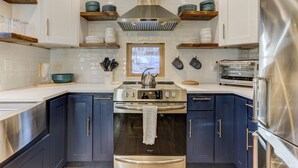 Una cocina moderna con electrodomésticos de acero inoxidable, armarios azul oscuro y estantes de madera.