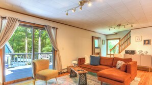 Una sala de estar con sofá, sillón y mesa de centro, una escalera y vistas al exterior.