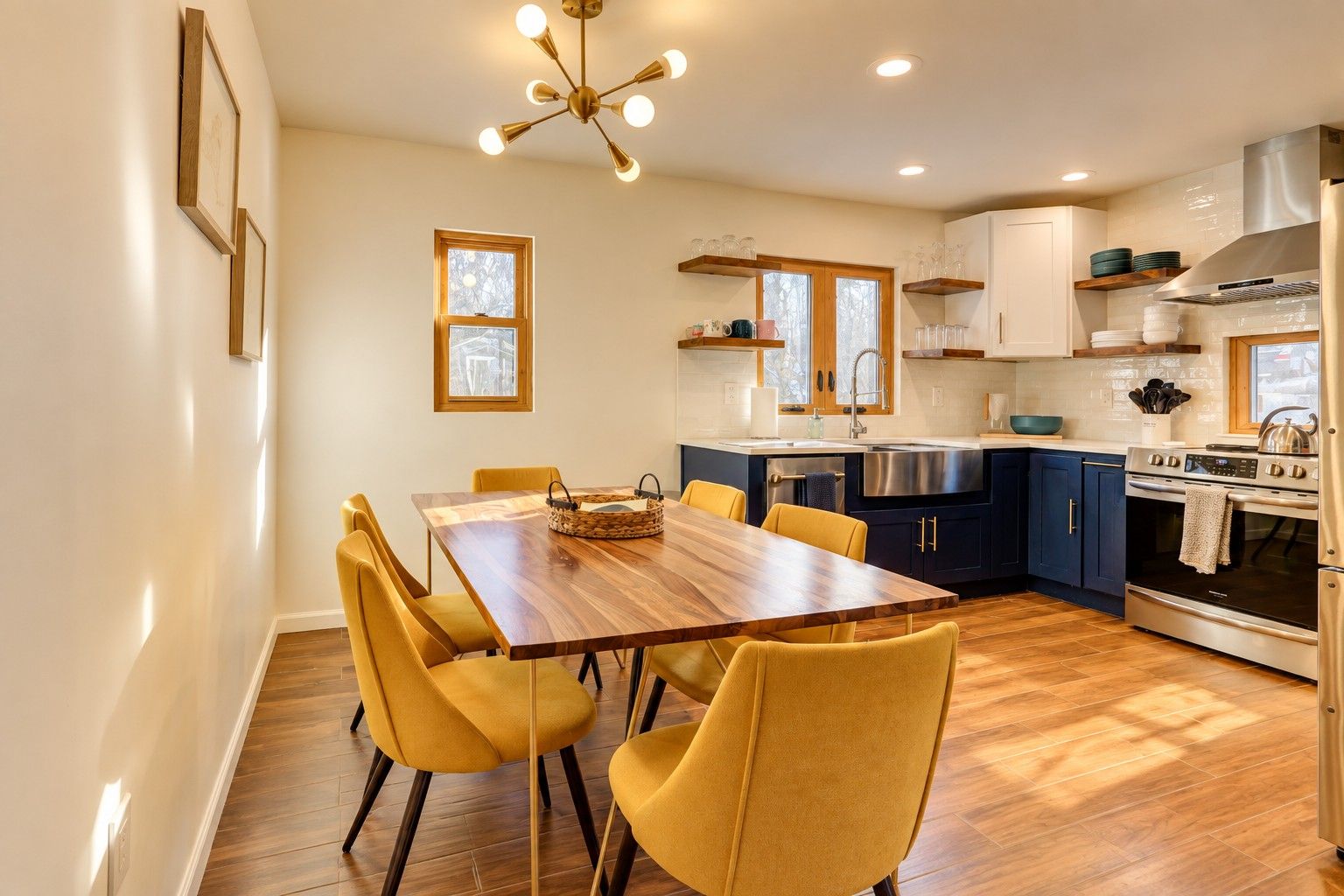 A modern kitchen with a wooden dining table, yellow chairs, and stainless steel appliances.