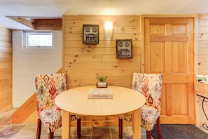 Un cuarto acogedor con paredes de madera, una mesa redonda, dos sillas estampadas, una puerta y una ventana.