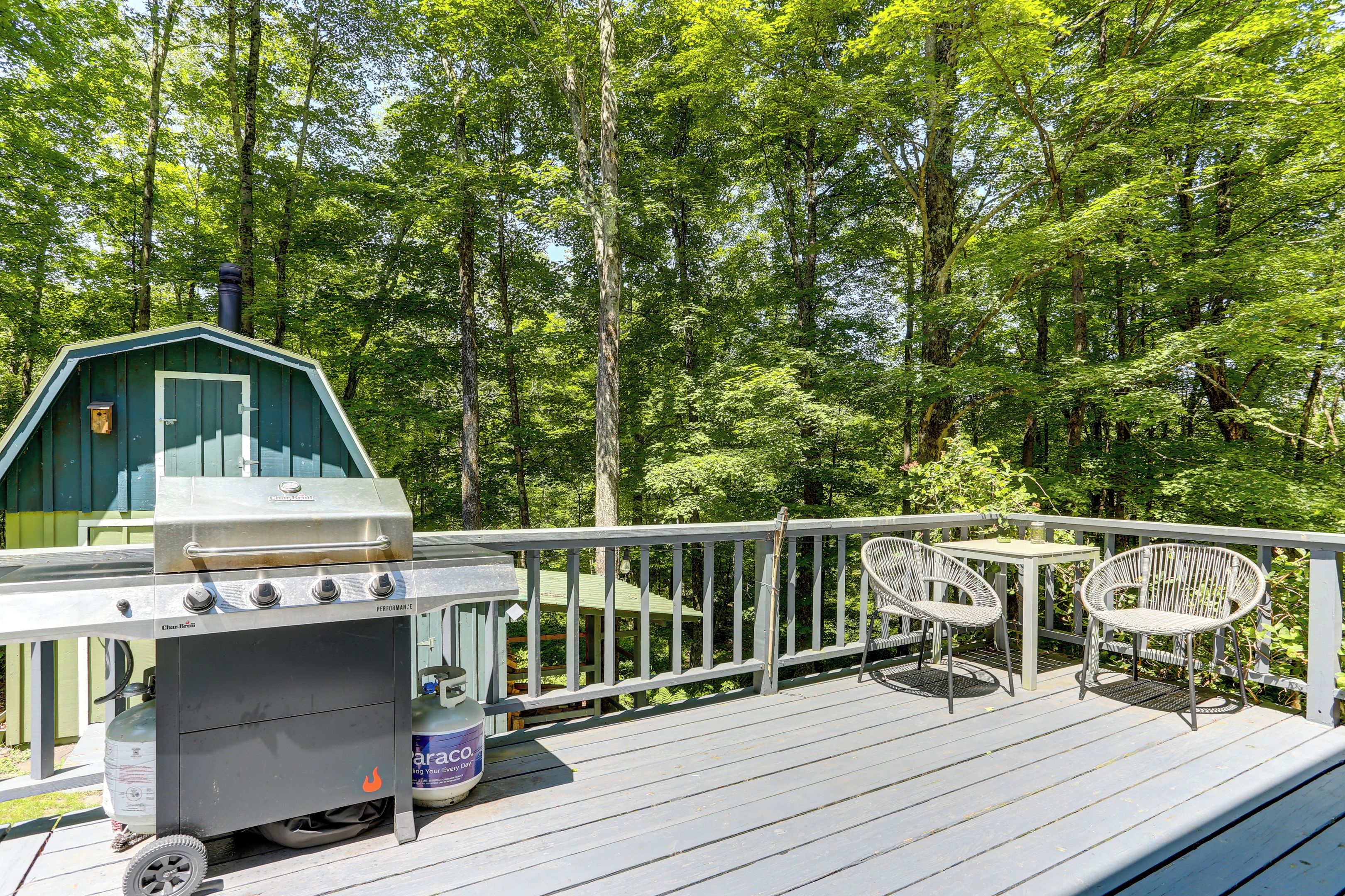 An outdoor deck with a grill, two chairs, and a small shed.