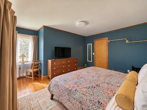 A bedroom with a bed, dresser, television, and a window with curtains.