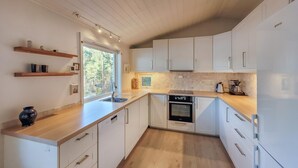 A modern kitchen with white cabinets, a dishwasher, an oven, and a coffee maker. There is a window providing natural light and a view of trees outside. - 2 bedroom cozy home in Jørpeland (Jørpeland)