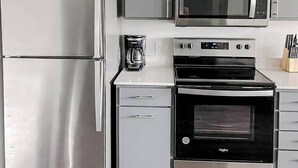 A modern kitchen with stainless steel appliances, including a refrigerator, microwave, and oven, and white cabinetry. - Sleepover | Picturesque 1BD/1BA - Des Moines (West Des Moines)