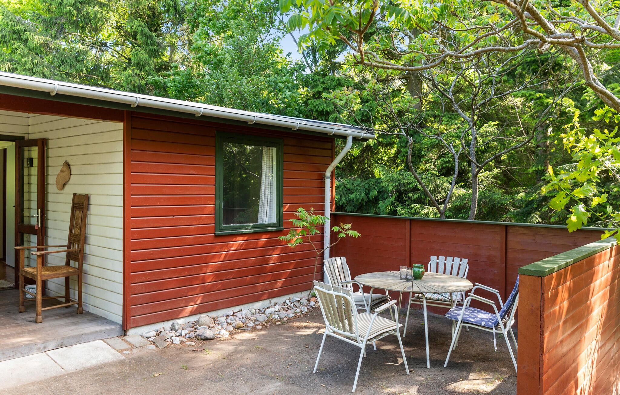 Una piccola baita di legno con un patio arredato con tavolo e sedie, immersa nel verde.