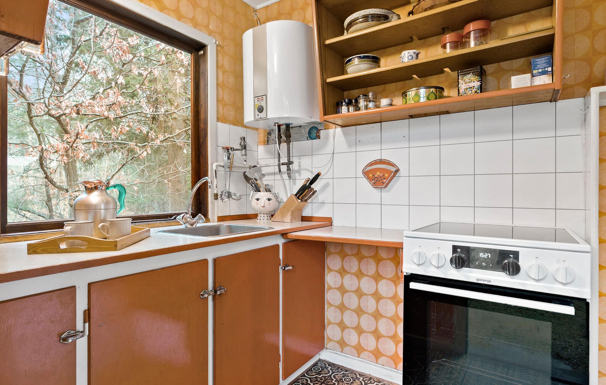 A kitchen with a window, a stove, and shelves with kitchenware.
