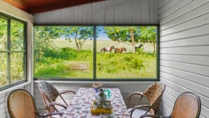 Een kamer met een groot raam met uitzicht op een grasveld met paarden. Er staat een tafel met stoelen en een koffiepot op.