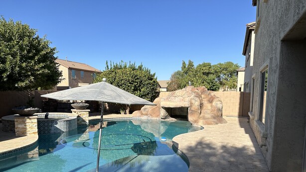 Une piscine agrémentée d’un élément rocheux, d’un mur en pierre et d’une terrasse carrelée.
