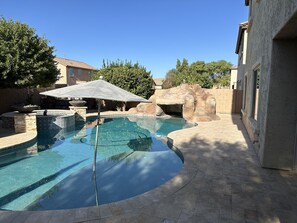 A swimming pool with a rock feature, a stone wall, and a tiled deck.
