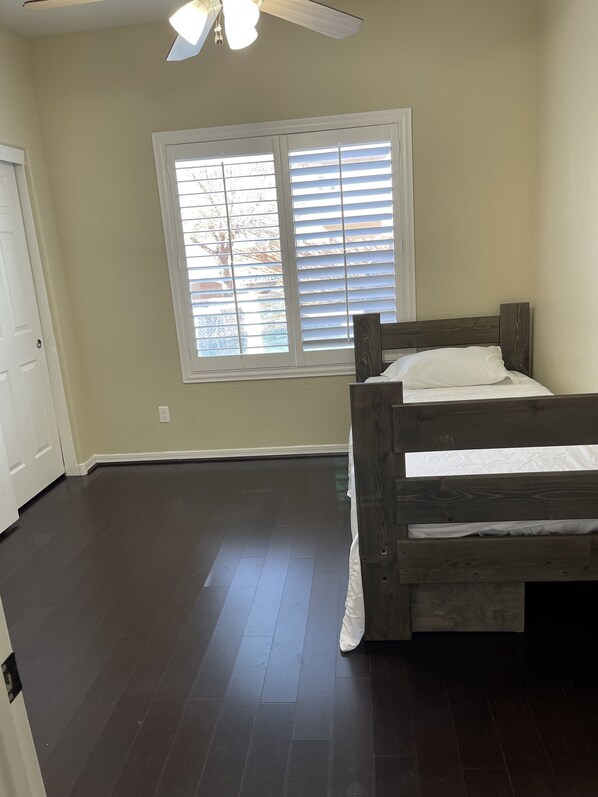 A bedroom with a wooden bed, a window with blinds, a ceiling fan, and a door.