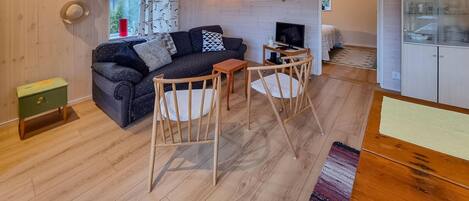 A cozy living room with a sofa, two wooden chairs, a small table, and a TV.
