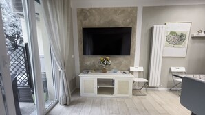 Une chambre moderne avec une grande télévision, un bureau agrémenté d’un vase de fleurs et une table de jeux.