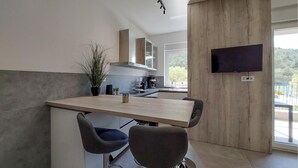 Eine moderne Küche mit einer Holztischinsel, zwei Barhocker, einem an der Wand montierten Fernseher und Blick ins Freie.