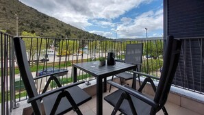 Ein Balkon mit Tisch und Stühlen mit Blick auf einen Parkplatz und eine hügelige Landschaft.