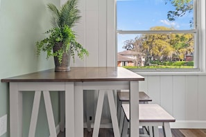 Sit and enjoy the view from this room's large window, which frames a tranquil residential area with trees and houses.
