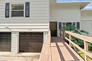 Two-story home with a garage and deck, surrounded by lush greenery.