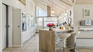A modern kitchen with a central island, bar stools, and a large window providing natural light. - Stunning home in Gilleleje with sauna (Gilleleje)