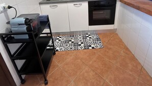 Een kleine keuken met witte kastjes, een gasfornuis, een inbouwoven en een zwart-wit gebonden vloerkleed.