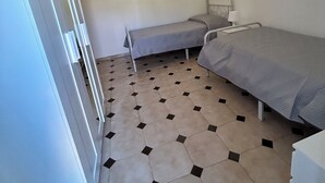 Een kleine, eenvoudig ingerichte kamer met twee eenpersoonsbedden, een witte kast en een betegelde vloer.