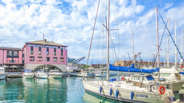 Un port de plaisance avec plusieurs bateaux amarrés, un bâtiment rose et un ciel dégagé.