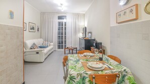 Un coin repas avec une table dressée pour deux personnes, un canapé et un téléviseur en arrière-plan.