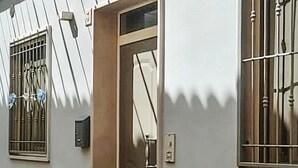 Un edificio con ventanas de rejas, una puerta con manija y una lámpara fijada a la pared.