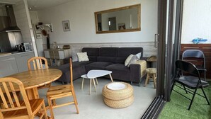 A living room with a sofa, coffee table, and chairs. There is a kitchen area with a stove and cabinets. A large mirror hangs on the wall.