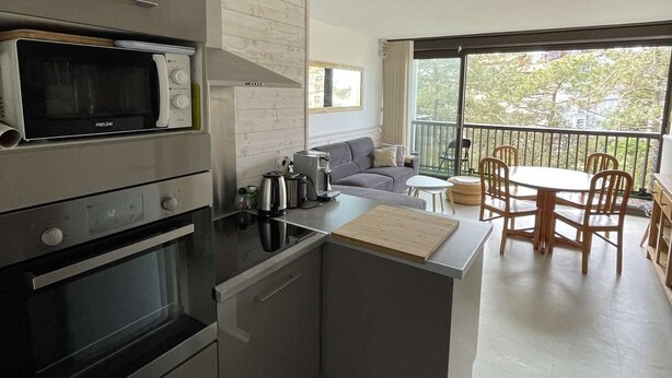 A modern kitchen with built-in appliances, a dining area with a table and chairs, and a balcony with a view.