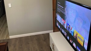 Ein Wohnzimmer mit einem Flachbildfernseher auf einem Schrank, einem Gemälde mit Strandmotiv und einer Holztür.