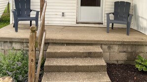 Eine Veranda mit zwei Adirondack-Stühlen, einer Betontreppe und einer Tür, auf der die Nummer 2 steht.