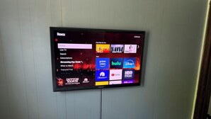 Ein flachbildfernseher an der Wand, der eine Roku-Oberfläche mit verschiedenen Streaming-Apps anzeigt.