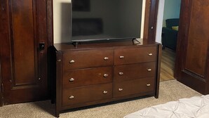 Ein Schlafzimmer mit einem hölzernen Schminktisch, einem Flachbildfernseher, einem Bett und einem Teppichboden.