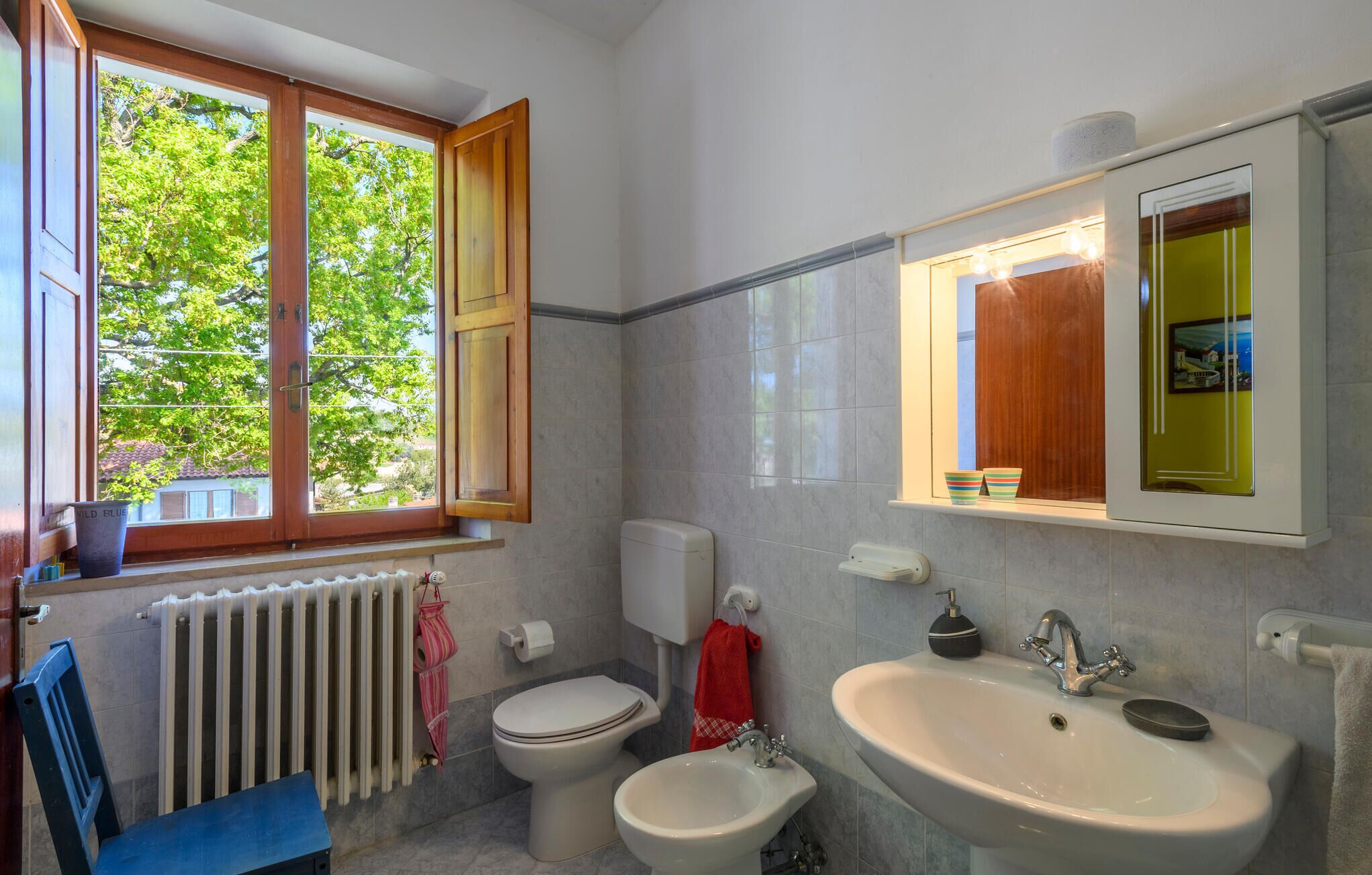 Un baño con inodoro, bidé, lavamanos y una ventana con vista a árboles.