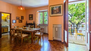 A dining room with a wooden table and chairs, a radiator, and a window with a view of trees.