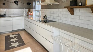 Une cuisine moderne avec des armoires blanches, un comptoir noir et une cuisinière encastrée. Un tapis à motifs étoilés recouvre le sol, et une étagère contenant des ustensiles de cuisine est placée au-dessus du comptoir.