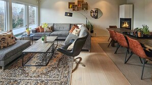 Un salon moderne avec un canapé, un fauteuil et une table à manger. On y trouve une cheminée et une grande fenêtre.