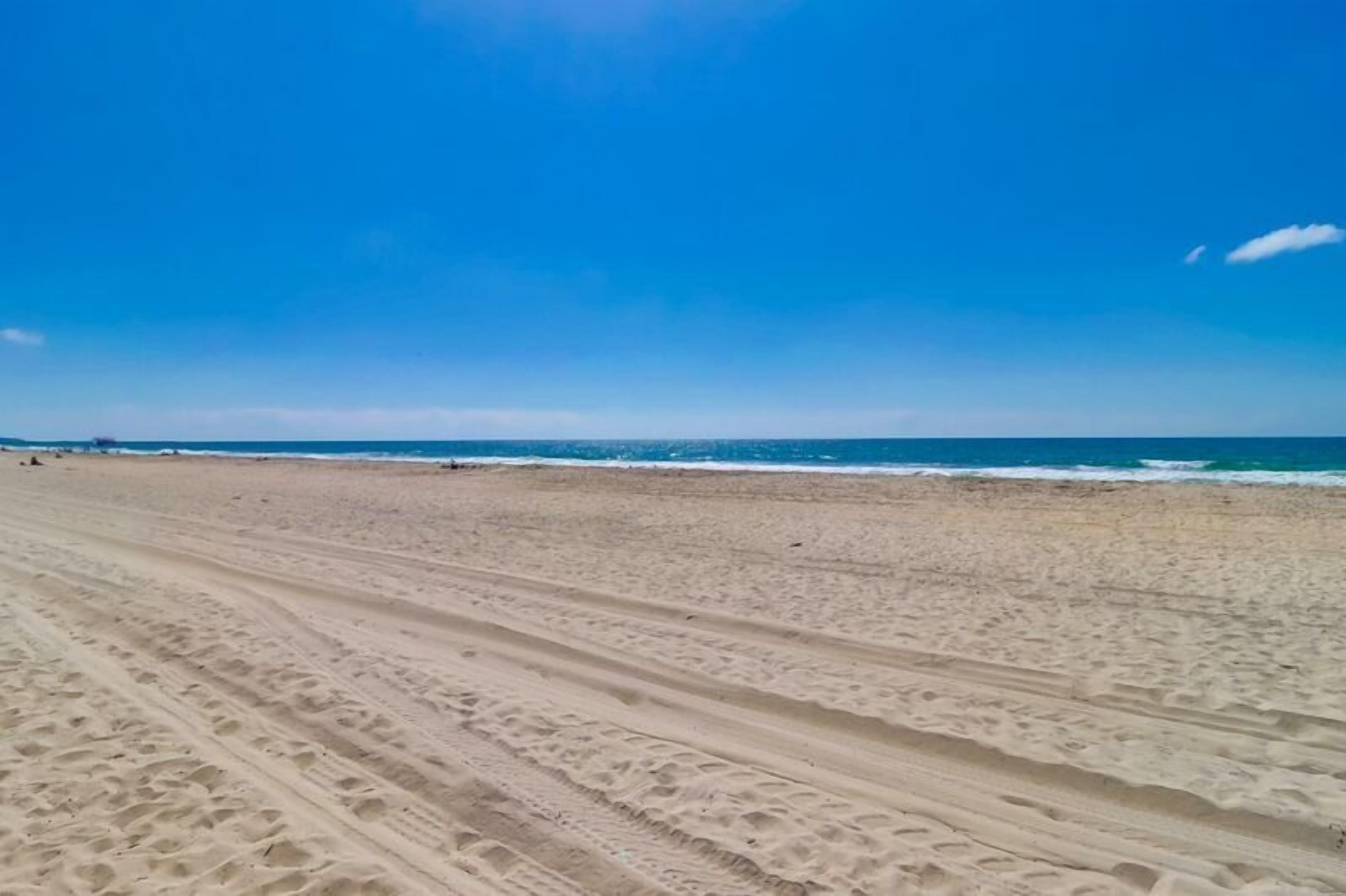 Une vaste plage de sable où l’on peut voir des traces de pneus, qui mènent à l’océan.