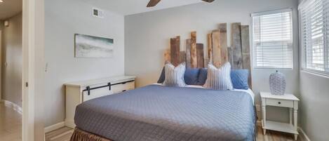 Une chambre à coucher avec un grand lit, un ventilateur de plafond, une table de chevet et une fenêtre avec des stores.