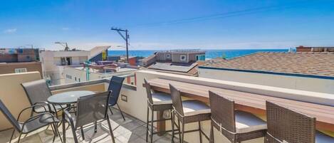 A rooftop terrace with a table and chairs, overlooking a coastal area.