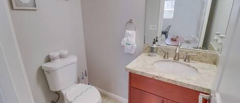 A bathroom with a toilet, sink, and mirror. There are framed pictures on the wall and a ceiling fan.