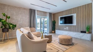 Un salon moderne avec un canapé, un pouf et un téléviseur à écran plat fixé à un mur en bois.