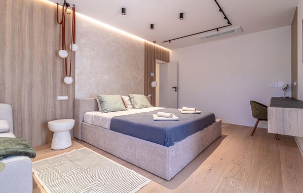 Quarto moderno com uma cama grande, mesas de cabeceira, escrivaninha e uma cadeira.
